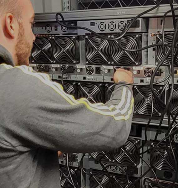 Hamus staff is operating the power switch on a Bitcoin miner, symbolizing the immediate start of miner hosting services at Hamus Hosting.