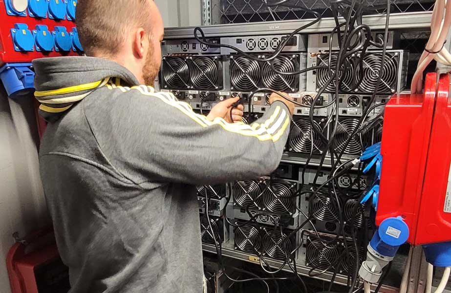 An individual operating the power switch on a Bitcoin miner, symbolizing the immediate start of miner hosting services at Hamus Hosting.