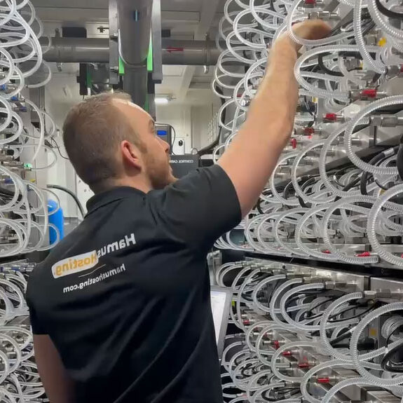 A glimpse into high-performance mining at Hamus Hosting! 💪 A professional, proudly wearing a Hamus Hosting shirt, connects an internet cable to a miner inside a Bitmain HK3 hydro container, surrounded by S19 Hydro miners—cutting-edge equipment built for maximum efficiency. 🚀⚡ #MiningHosting #BitmainHK3 #HamusHosting #HighPerformanceMining
